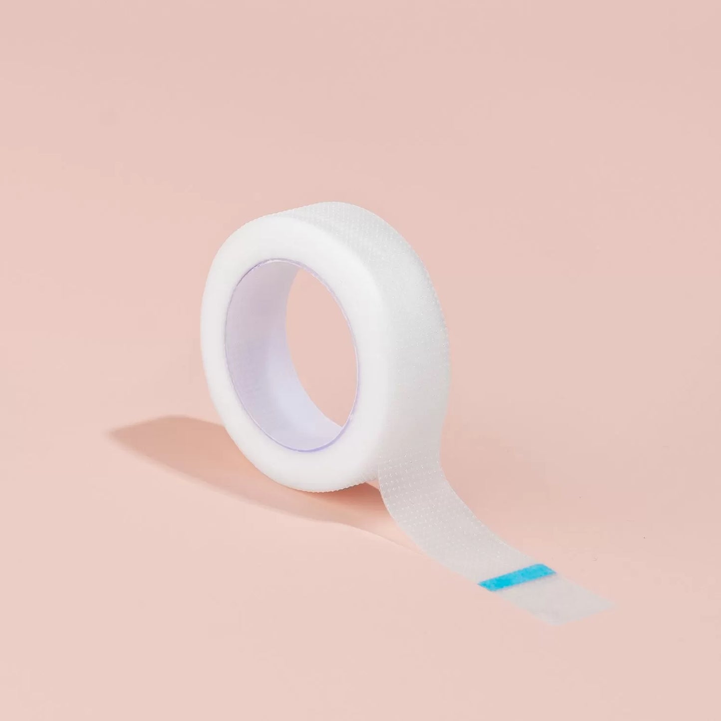 Dettaglio ravvicinato del rotolo di nastro adesivo in plastica Barbara parzialmente srotolato, che mostra la superficie microforata per una facile rimozione, su sfondo rosa.